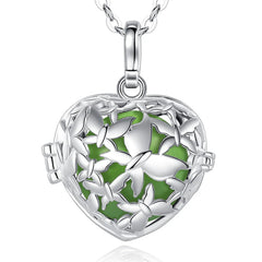 A silver heart-shaped locket pendant necklace with a green enamel background and butterfly details, shown on a white background with a faint reflection.