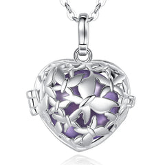 Silver heart-shaped locket pendant necklace with butterfly detailing and a lavendaer enamel center, shown on a white background with a faint reflection.