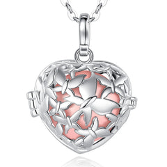 A silver heart-shaped locket pendant necklace with a butterfly cutout design and a peach enamel background, shown on a white background with a faint reflection below.