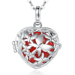 A silver heart-shaped locket pendant necklace with a red sphere inside it and silver butterfly cutout detailing, shown on a white background with a faint reflection below.