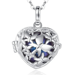 A silver heart-shaped locket pendant necklace with a butterfly cutout design and a blue purple glittery interior, shown on a white background with a reflection.