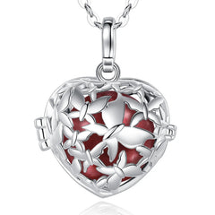 A silver heart-shaped locket pendant necklace with a butterfly design and a sienna enamel background, shown on a white background with a faint reflection below.