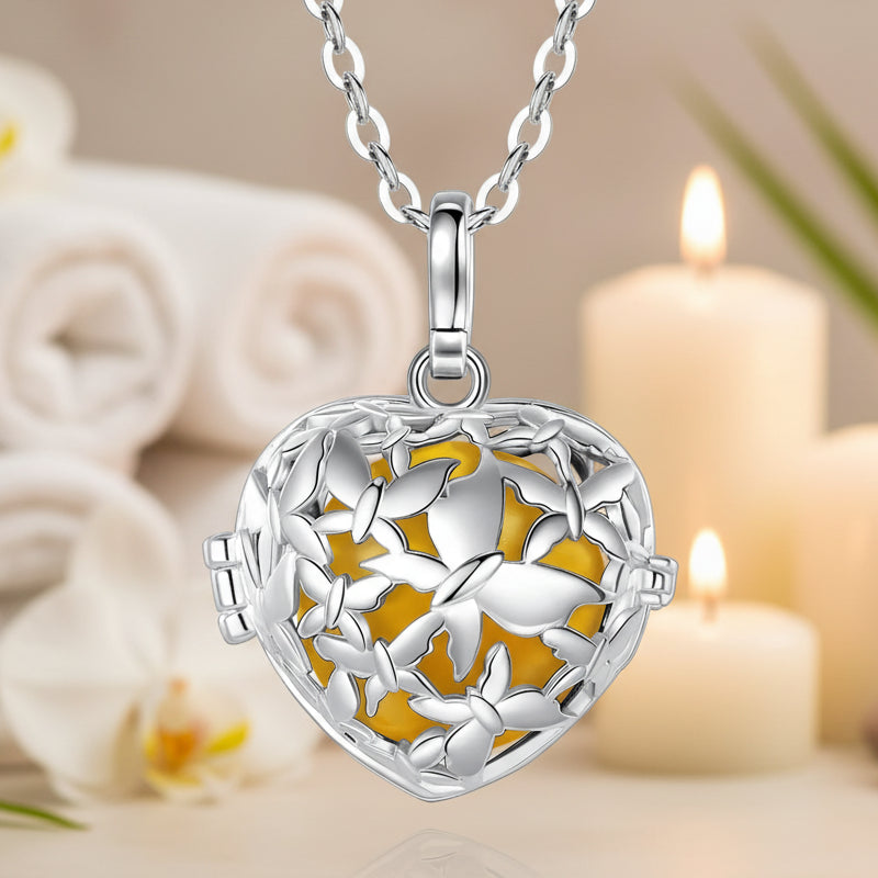 A heart-shaped silver locket pendant necklace with a butterfly design and a vibrant yellow-orange enamel background, shown on a white background with a subtle reflection.