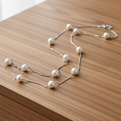 Sterling silver station necklace with evenly spaced micro‑pearls displayed on a wood furniture background.