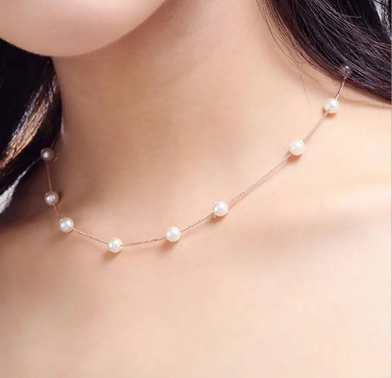 Sterling silver station necklace with evenly spaced micro‑pearls worn with a light neutral top.