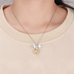 A close-up of a person wearing a sterling silver dragon pendant necklace with a round yellow pearl inside, paired with a beige crewneck sweater.