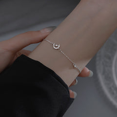 Silver bracelet with a heart charm on a wrist against a neutral background