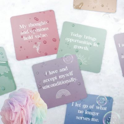 Waterproof shower affirmation cards displayed with water droplets, featuring pastel backgrounds and uplifting quotes for daily positivity and mindfulness.