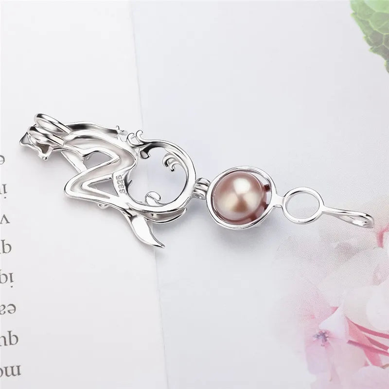 A silver pendant featuring a stylized abstract figure with a round, lustrous pearl-like brown gemstone, displayed on a light background with soft pink floral elements.