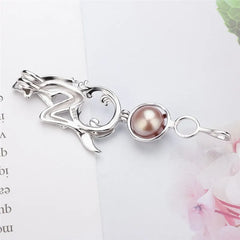 A silver pendant featuring a stylized abstract figure with a round, lustrous pearl-like brown gemstone, displayed on a light background with soft pink floral elements.