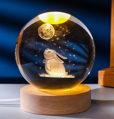 Crystal ball with rabbit and moon design on a wooden base against a dark blue background