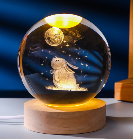 Crystal ball with rabbit and moon design on a wooden base against a dark blue background