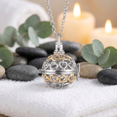 A two-tone silver and gold heart-shaped locket pendant necklace on a white towel and stones background.