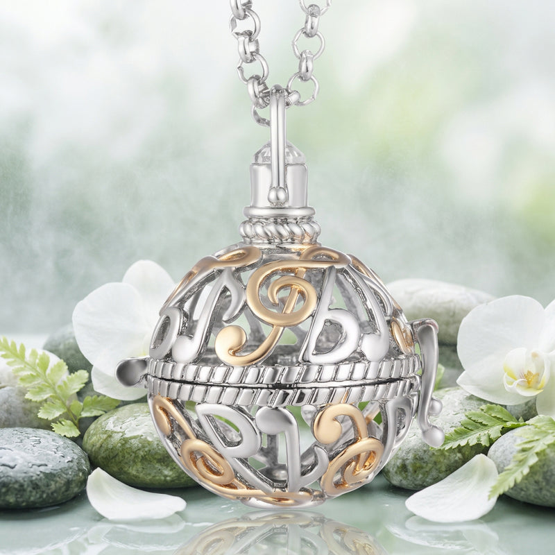 A silver and gold ball-shaped locket pendant necklace featuring musical notes and treble clefs, suspended from a silver link chain against a light green and white orchids background.