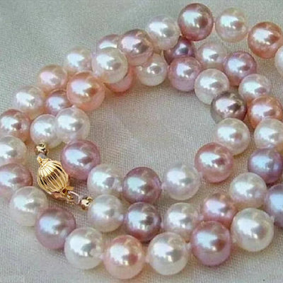 A strand of freshwater pearls in shades of pink, lavender, and white, featuring a gold-toned toggle clasp, displayed on a neutral beige fabric background.