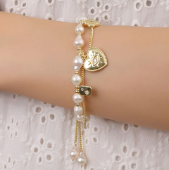 Pearl bracelet with gold heart charm on a wrist against a white lace background