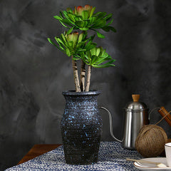 Green succulent rosettes on tall stems in a textured black vase beside a metal kettle.
