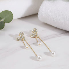 Pair of earrings with heart-shaped tops and pearl drops on a white surface.