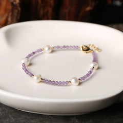 Light purple faceted beaded bracelet with round white pearls and gold spacer beads, displayed on a white ceramic dish.