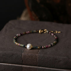 Multicolor beaded fashion bracelet featuring small round beads in pink, green, blue, and gold with a single white pearl accent, displayed on a textured stone surface.