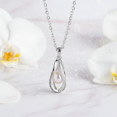 Elegant silver teardrop necklace with a white pearl and gemstone accents displayed beside soft orchid flowers.