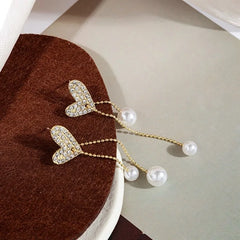 Heart-shaped earrings with pearl drops on a brown fabric background