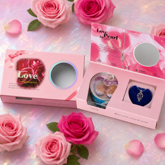 Pink rose-themed pearl gift boxes with an oyster tin and silver-tone cage necklace, arranged among roses.