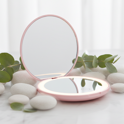 A compact, round lighted makeup mirror with a soft pink frame, shown open against a solid white background.