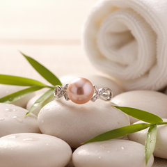 Pink freshwater pearl ring with a silver band and small diamond accents displayed on smooth white stones with bamboo leaves in a serene spa-style setting.