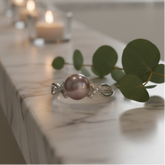 Purple freshwater pearl ring with an intricate silver band and gemstone accents displayed on a marble surface with eucalyptus leaves and softly lit candles