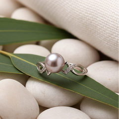 Purple freshwater pearl ring with an elegant silver band and small crystal accents displayed on a green leaf over smooth white stones in a soft, natural setting.