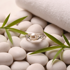 Freshwater pearl ring with a silver band and delicate side details displayed on smooth white stones with bamboo leaves and a soft spa-style background.