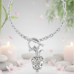 Elegant silver apple-shaped pendant necklace with a pearl inside displayed in a serene spa-inspired setting with candles, stones, and pink petals.