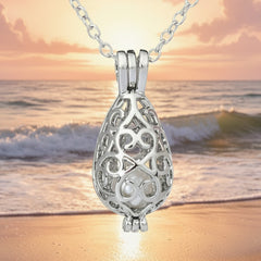 Elegant silver filigree teardrop pendant necklace featuring a central pearl displayed against a serene beach sunset background.