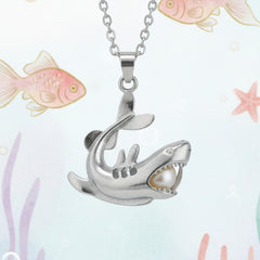 Silver shark-shaped pendant necklace holding a pearl displayed against a playful underwater-themed background.