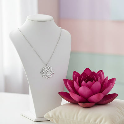 A silver lotus flower pendant necklace on a delicate silver chain, shown next to a magenta lotus flower.