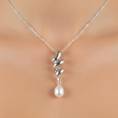 A silver spiral pendant necklace with a single white pearl drop, displayed on a neckline.