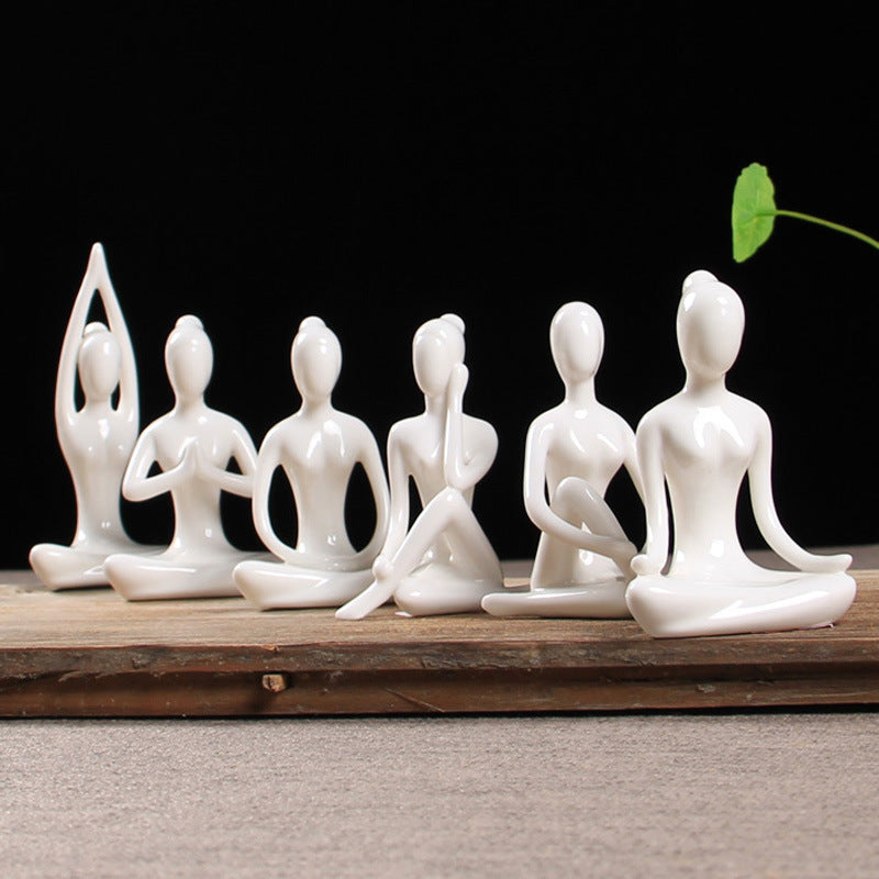 Six white ceramic female figurines in different seated yoga poses arranged on a wooden board.