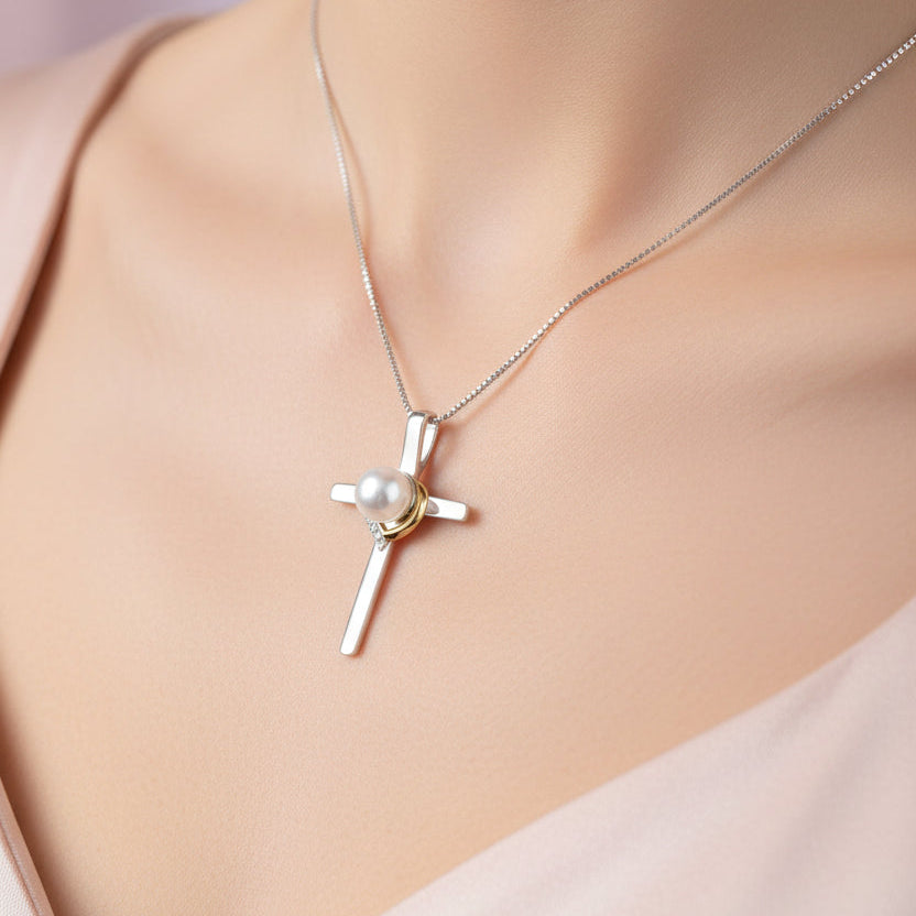 A sterling silver cross pendant necklace with a white pearl and a small gold accent, displayed on a beige skin.