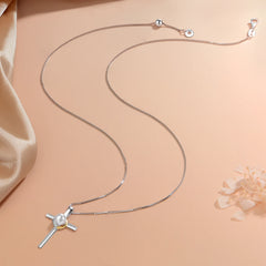 A silver cross pendant necklace with a central white pearl, displayed on a peach-colored background with a satin fabric prop and a decorative flower.