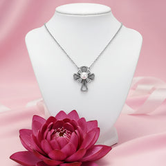 A sterling silver cross pendant necklace with a central white pearl and small clear stones, displayed on a soft pink satin background.