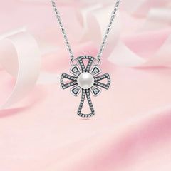 A sterling silver cross pendant necklace with a central white pearl and small clear stones, displayed on a soft pink satin background.