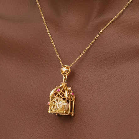 A sterling silver gold-toned necklace with a detailed birdcage pendant featuring small pink gemstones displayed on a darker skinned model neckline