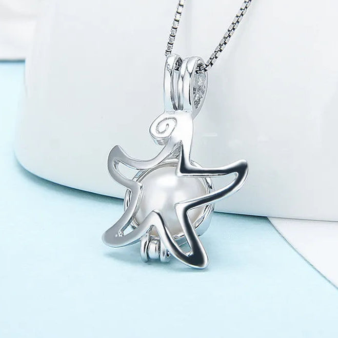 A sterling silver starfish pearl cage with a glossy white pearl in its center, hanging from a fine chain against a soft white and pale blue studio background.