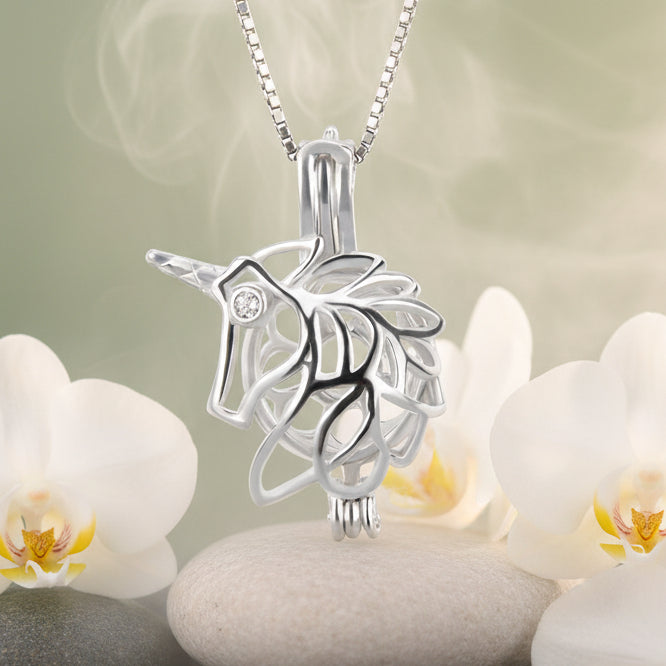 A sterling silver unicorn pearl cage pendant with a delicate chain, shown in front of white orchids and white stones background.