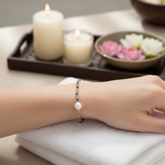 Tourmaline multicolor beaded bracelet with a single pearl centerpiece worn on a wrist resting on a white towel in a spa‑style setting with candles and flowers in the background.
