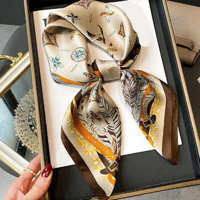 Silk-like square scarf with feather, belt, and floral pattern displayed folded in a gift box