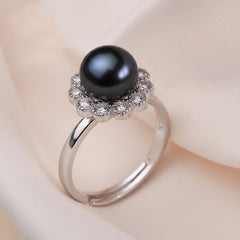 Sterling silver ring featuring a natural black freshwater pearl with a sparkling gemstone flower halo displayed on a soft fabric background.