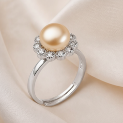 Sterling silver ring featuring a soft champagne‑gold freshwater pearl with a sparkling gemstone flower halo displayed on a cream fabric background.