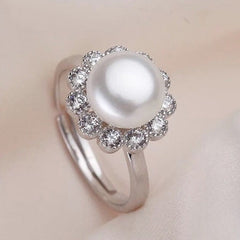Sterling silver ring featuring a white freshwater pearl with a sparkling gemstone flower halo on a soft fabric background.